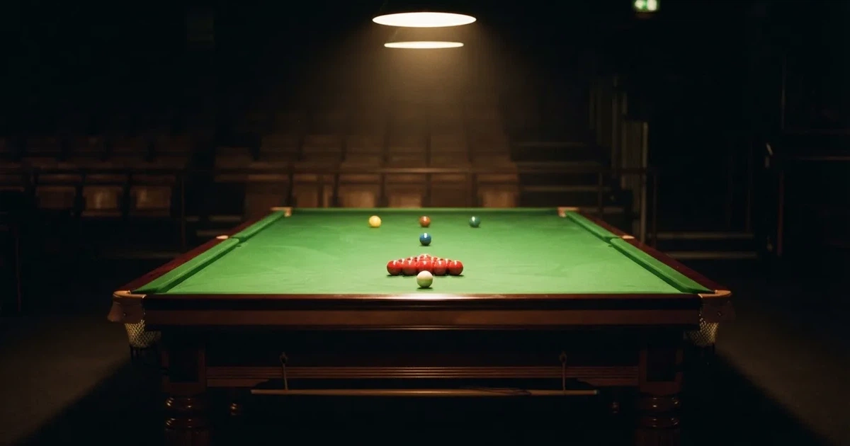 Ein Snookertisch mit grünem Tuch in einem abgedunkelten Saal, ein Lichtkegel fällt von oben auf die aufgestellten Kugeln.