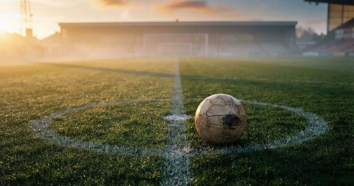 Ein Fußball liegt auf der Mittellinie eines leeren Rasenplatzes, die Kreidelinie verläuft scharf durchs Bild im Morgenlicht.